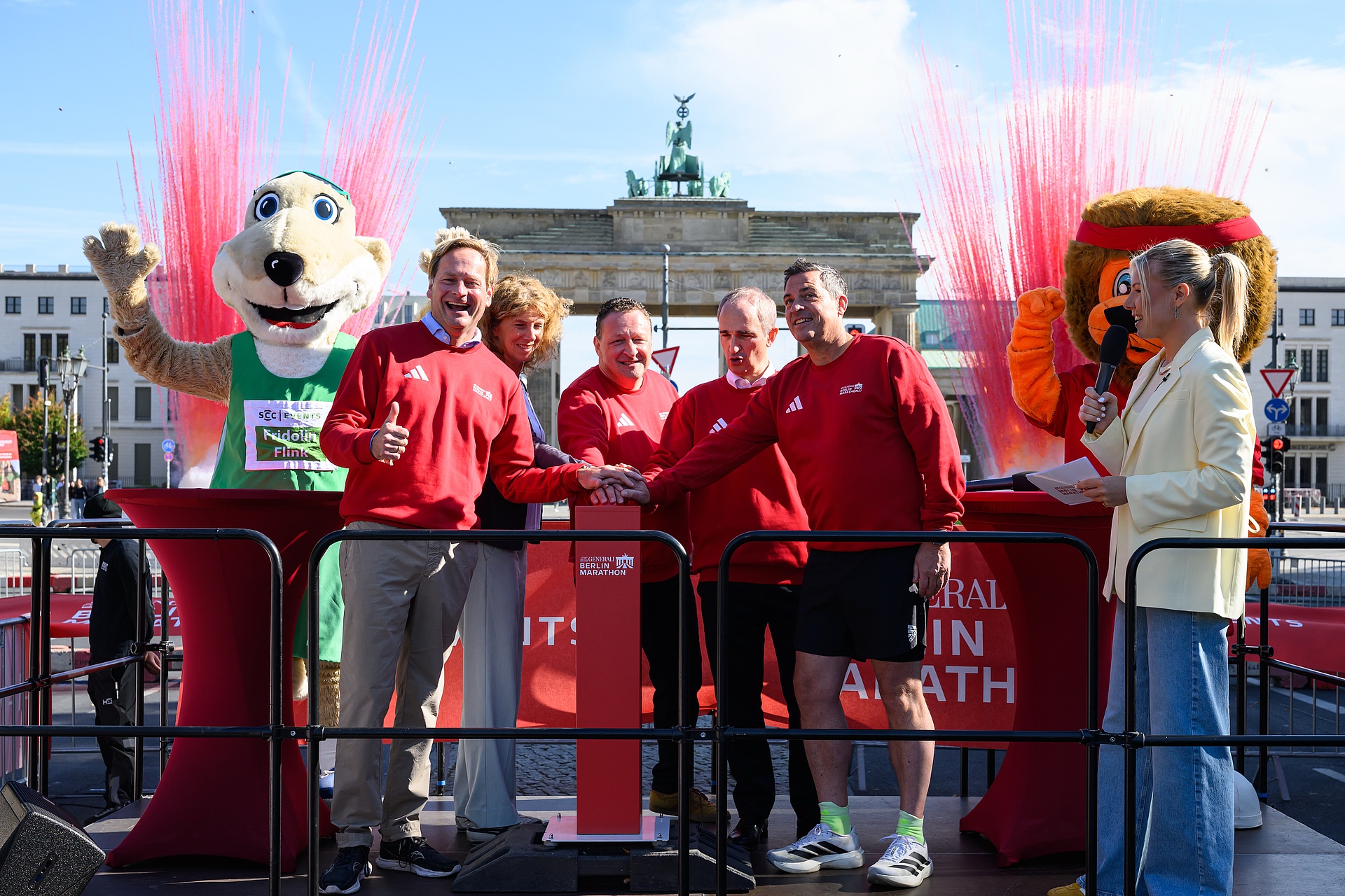 Die Führungsebene von SCC Events, in rot gekleidet vor dem Brandenburger Tor drücken fröhlich gemeinsam zu fünft den Startknopf für die Registrierung zum GENERALI BERLIN-Marathon 2027.