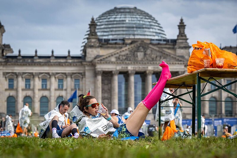 Finisherin des Marathons liegt vor dem Reichstag, trinkt etwas und hat ihre Beine hochgelegt.
