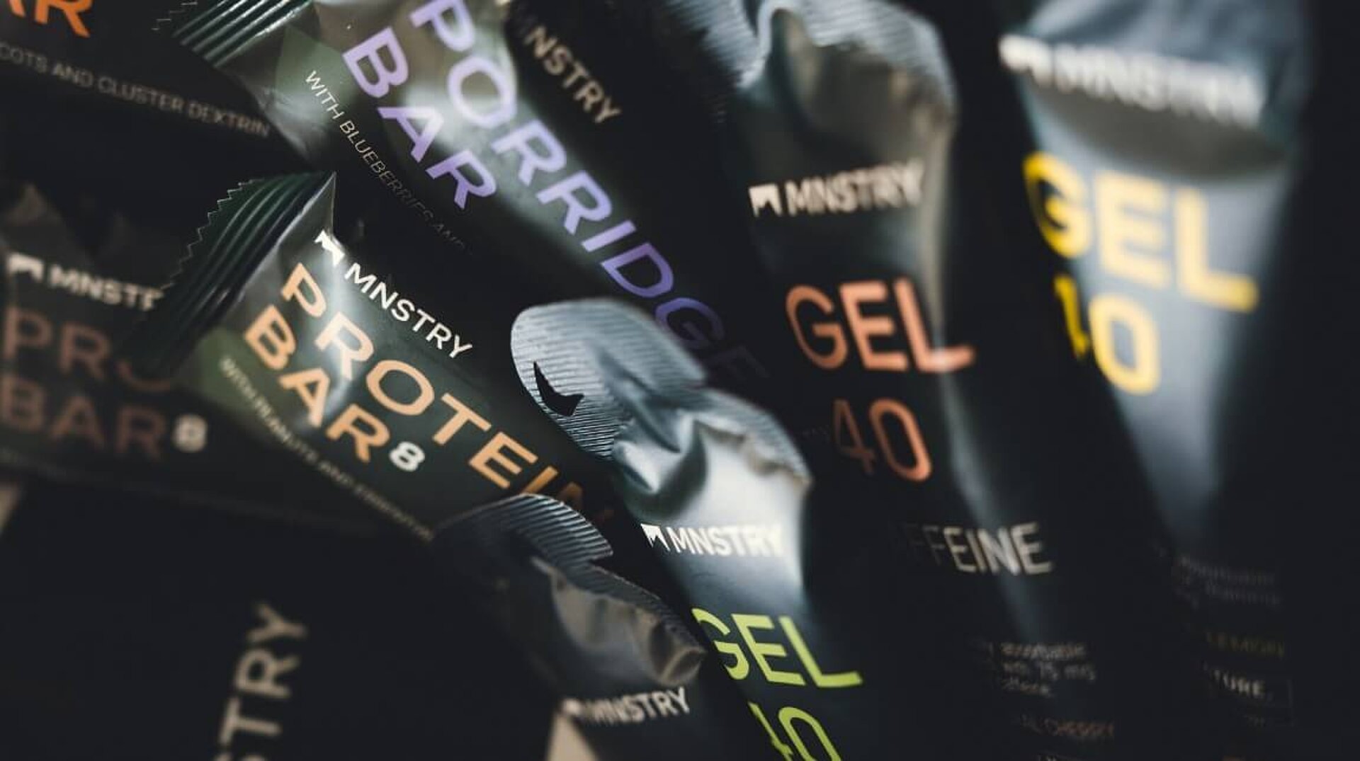 Nahaufnahme verschiedener MNSTRY-Produkte, darunter Protein-Riegel, Porridge-Riegel und Gels.